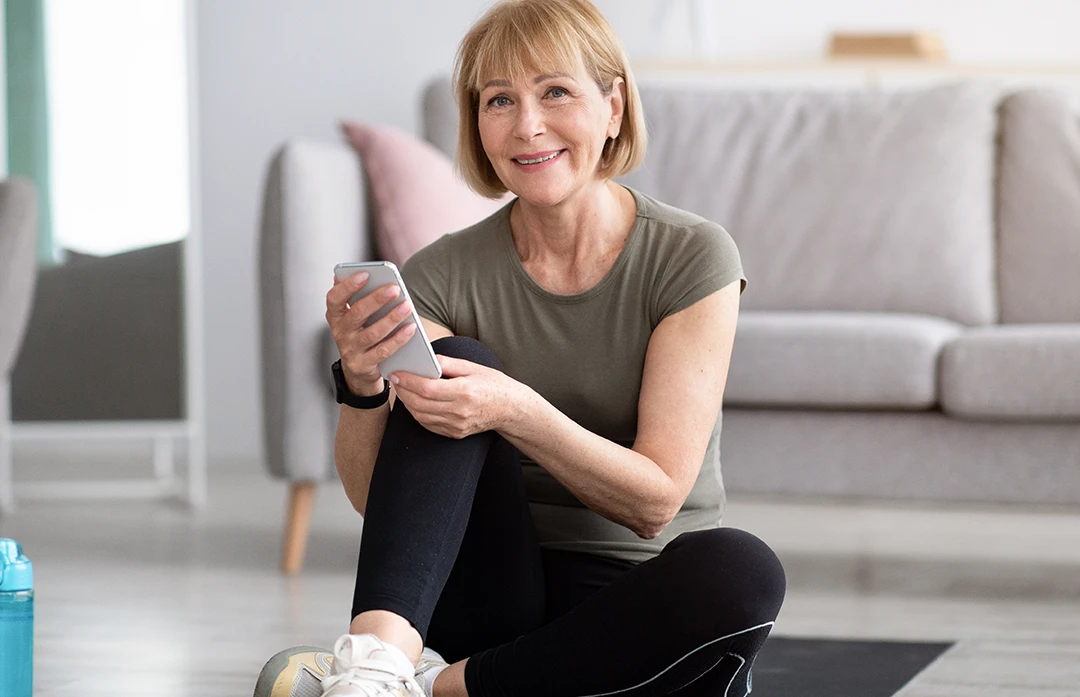 Mature-age Woman smiling, sitting on living room floor, learning about Bladder Prolapse