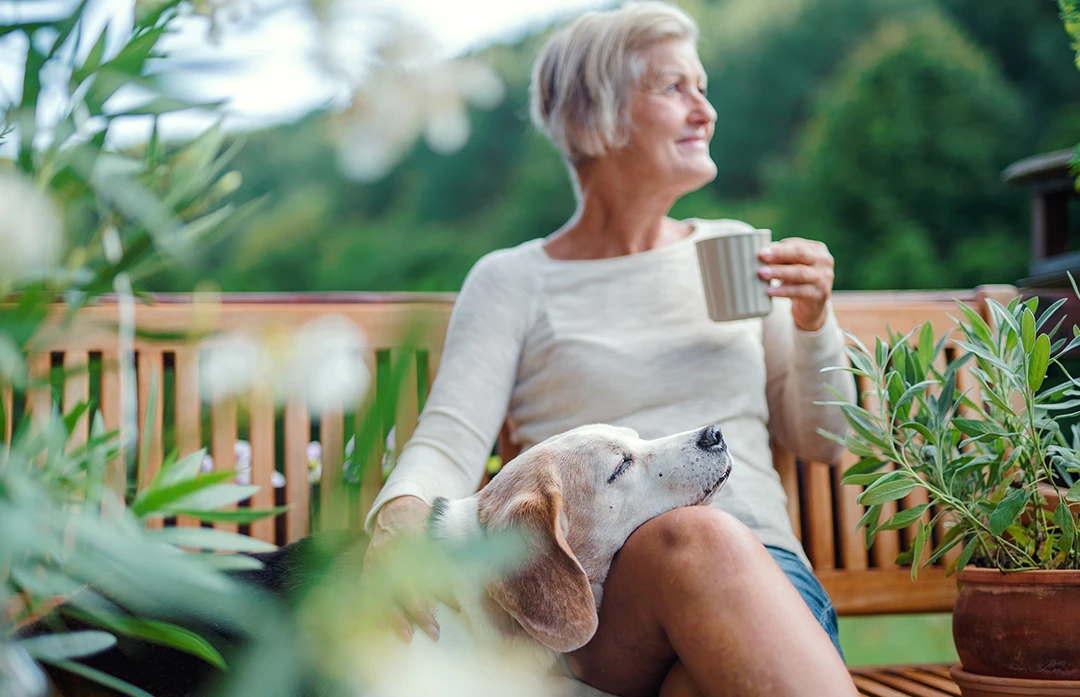 Mature-age Woman smiling, petting dog on outside bench, dealing with Mixed Incontinence